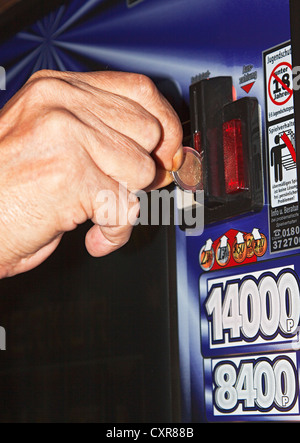 Die Hand eines Mannes ist eine Euro-Münze einfügen in ein Spielautomat, Warnschild, Spielsucht Stockfoto