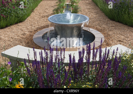 Moderner englischer Kiesgarten mit Wasser aus Edelstahl mit Brunnen und Gartenbank aus Rill-Stein grenzt an England UK Stockfoto