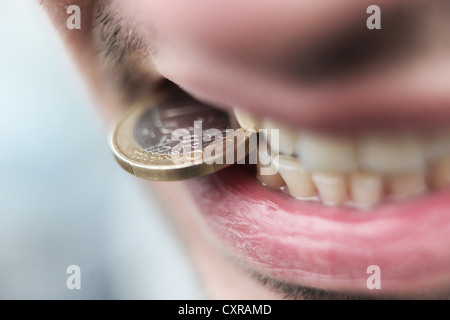 Mann mit ein-Euro-Münze zwischen den Zähnen, symbolisches Bild für die Euro-Krise Stockfoto