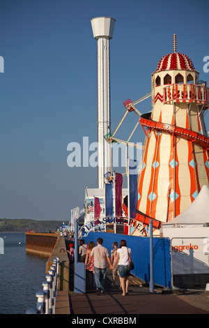 Besucher, die zum Pleasure Pier in Weymouth, Dorset UK, zum Sea Life Tower, zum Jurassic Skyline Tower, vorbei an einer helter Skelter Fairground Ride fahren Stockfoto