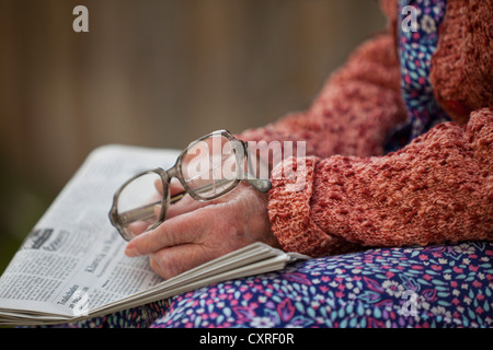 Hände einer alten Frau hält alte zerbrochene Gläser auf einer Zeitung Stockfoto