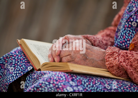 Hände einer alten Frau liegend auf dem Schoß auf ein offenes Buch Stockfoto