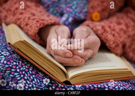 Hände einer alten Frau liegend auf dem Schoß auf ein offenes Buch Stockfoto