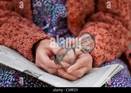 Hände einer alten Frau hält alte zerbrochene Gläser auf einer Zeitung Stockfoto