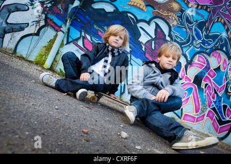 Zwei jungen, 5 und 7 Jahren, sitzen auf einem Skateboard vor einer Wand mit graffiti Stockfoto