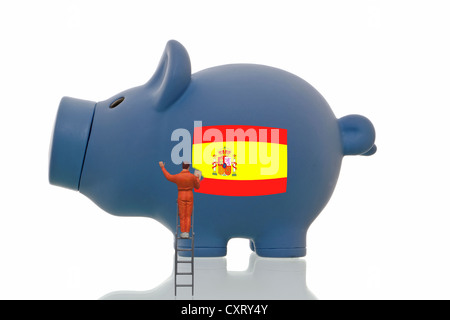 Miniaturmalerei Figur über eine spanische Nationalflagge auf ein blaues Sparschwein, symbolisches Bild Stockfoto