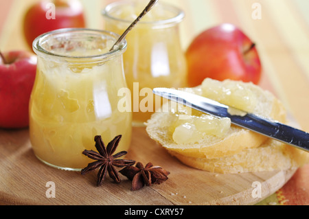 Gläser mit Apfel Marmelade mit Zimt und in Scheiben geschnittene Brot auf Schneidebrett Stockfoto