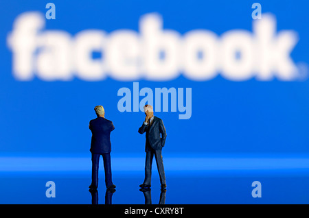 Zwei Geschäftsleute, Miniaturfiguren, steht man vor einem unscharfen Facebook-Logo, symbolisches Bild Stockfoto