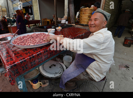 Sonntagsmarkt, Uyghur Senior mit einem traditionellen Hut Verkauf gehacktem Hammelfleisch, muslimische Basar, Uighur, Kashgar, Xinjiang, China Stockfoto