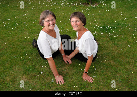 Zwei rüstige Zwillingsschwestern, die sitzen auf dem Rasen Stockfoto