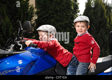 Zwei jungen, 4, trägt Schiebermütze sitzen zusammen auf einem blauen Motorrad Stockfoto