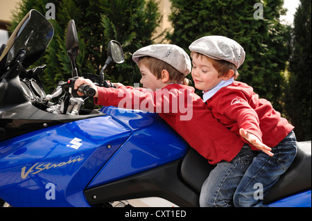 Zwei jungen, 4, trägt Schiebermütze sitzen zusammen auf einem blauen Motorrad Stockfoto