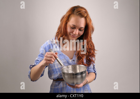 Junge Frau mit roten Haaren, die Mischung mit einem Schneebesen in einer Edelstahlschüssel Stockfoto