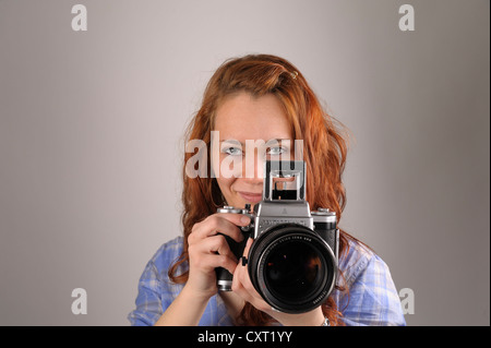 Junge Frau mit roten Haaren, die mit dem Fotografieren mit einer analogen Mittelformat-Kamera Pentacon Six Stockfoto