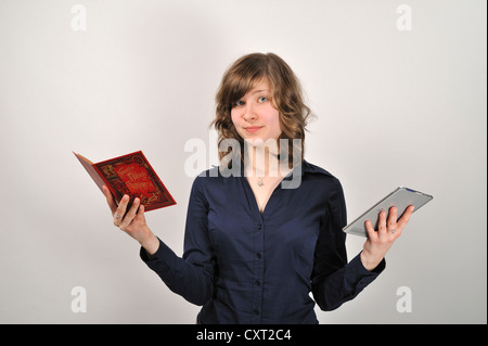 Junge Frau, 20, hält ein Buch in der einen Hand und ein digitales Buch, e-Book-Reader, in der anderen Stockfoto