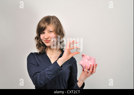 Junge Frau, 20, eine 10 Euro Silber Münze in ein rosa Sparschwein Stockfoto