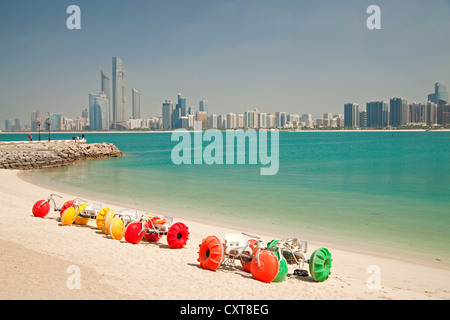 Bunte Tretboote am Strand vor dem Heritage Village, vor der Skyline von Abu Dhabi, Vereinigte Arabische Emirate Stockfoto