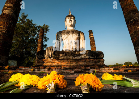 Blumen vor der sitzende Buddha-Statue im Wat Mahathat Tempel, Sukhothai Historical Park, UNESCO-Weltkulturerbe Stockfoto