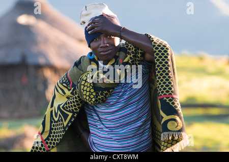 Basotho junge Mann trägt einen Tracht, eine Hütte auf der Rückseite, Drakensberge, Königreich Lesotho, Südafrika Stockfoto