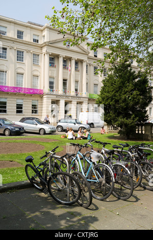 dh die Promenade CHELTENHAM GLOUCESTERSHIRE Girls sitzen entspannend auf Gras- und Fahrräder Fahrrad stehen städtische Ämter Stockfoto