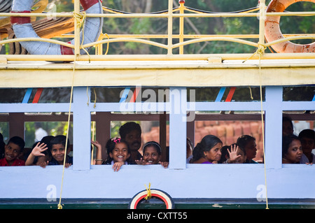 Horizontale Ansicht von Schulkindern winken und Lächeln von der öffentlichen Fähre in den Backwaters von Kerala. Stockfoto