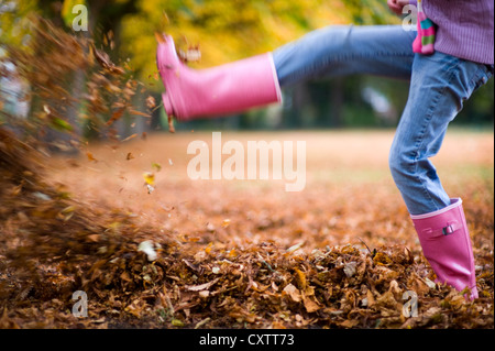 Mädchen in rosa Kaugummi Stiefel treten gefallenen Herbst oder Herbstlaub Stockfoto