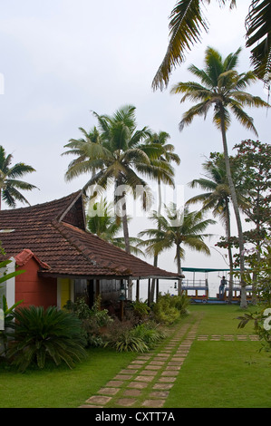 Vertikale Ansicht von Teak Holzbungalows in einem Resort in den Backwaters von Kerala, mit einem Ausflugsboot warten auf Kunden. Stockfoto