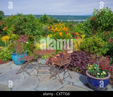 Maury-Vashon Island, WA: Eisen Sie, Tisch und Stühle auf Steinplatten Terrasse mit Blick auf einen terrassenförmig angelegten Garten und der Quartiermeister Hafen Stockfoto