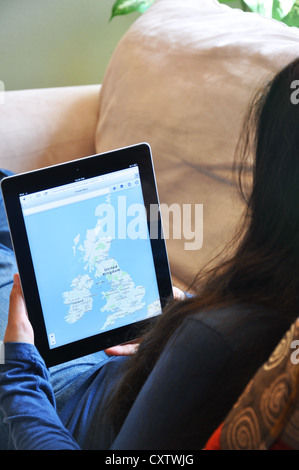 Junge Frau mit dem iPad auf dem Sofa zu Hause sitzen. UK-Karte auf dem iPad-Bildschirm angezeigt. Stockfoto