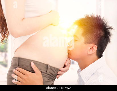 asiatischen Vater küssen seine schwangere Frau Bauch am Morgen Stockfoto