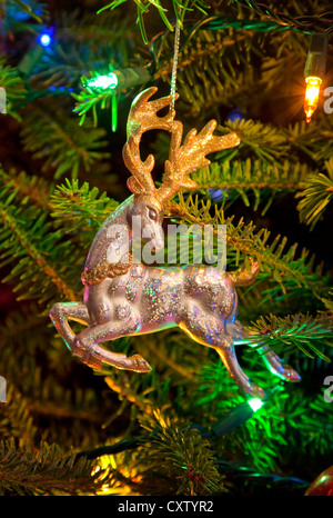 Ein glänzend metallische Rentier Hirsch Ornament in der umgeben von Weihnachtsbeleuchtung Weihnachtsbaum hängen. Stockfoto