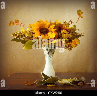 Eine herbstliche Bouquet mit getrockneten Sonnenblumen, Trauben und Blätter in einer Vase und trockene Blätter auf einem Holztisch Stockfoto