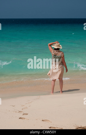 Eine Frau blickt auf einem schönen Meer von einem Sandstrand entfernt, Strohhut im Wind zu halten, auf Stockfoto