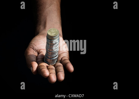 Indische mans Hand mit einem Stack von Rupie Münzen vor schwarzem Hintergrund Stockfoto