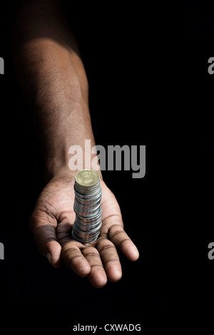 Indische mans Hand mit einem Stack von Rupie Münzen vor schwarzem Hintergrund Stockfoto