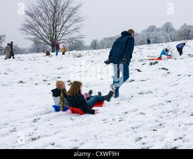 Genießen Sie den Schnee-Mann zog zwei Kinder auf Schlitten im Schnee Richmond Park im Winter, Richmond upon Thames, London, UK Stockfoto