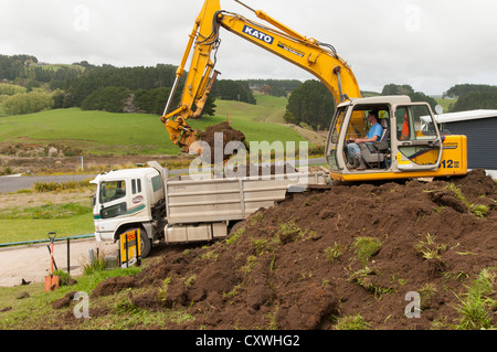 Mann ausheben Boden in LKW mit 12 Tonnen Bagger für neues Zuhause am steil abfallenden Abschnitt, umgeben von einer ländlichen Landschaft. Stockfoto