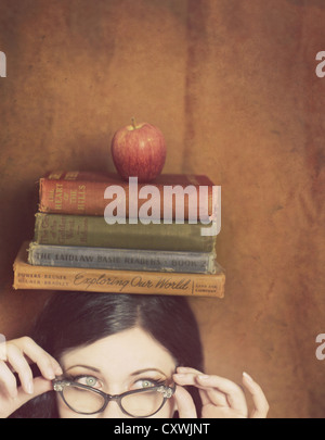 Partielle Gesicht einer jungen Frau trägt Vintage Brille und Blancing vier Bücher und einen Apfel auf dem Kopf Stockfoto