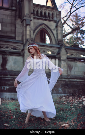 Zwirbelte Mädchen mit roten Haaren vor einer großen Burg trägt ein atemberaubende weiße Hochzeitskleid Stockfoto