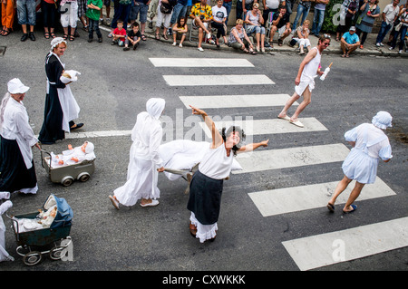 Singen & tanzen Darsteller verkleidet als Mutterschaft Krankenschwestern & Babys bei Autrefois Le Couserons Parade, St. Girons, Frankreich. Stockfoto