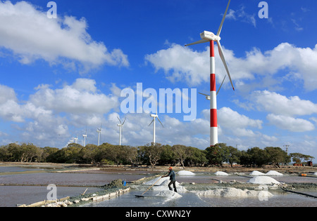 Arbeiter Rechen Salz in Stapeln auf Salz Bauernhof mit Windkraftanlagen im Hintergrund. Stockfoto