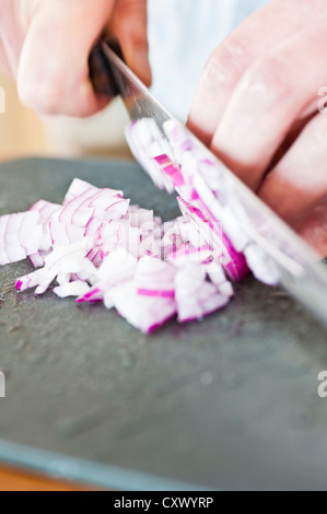 Nahaufnahme von roten Zwiebeln werden von einem Koch auf ein Kunststoff Schneidebrett gehackt Stockfoto