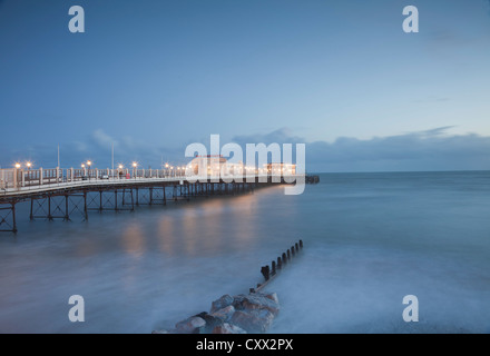 Abends Blick auf Worthing Pier, Sussex, bei Sonnenuntergang, mit Felsen und Buhne im Vordergrund beleuchtet. Stockfoto