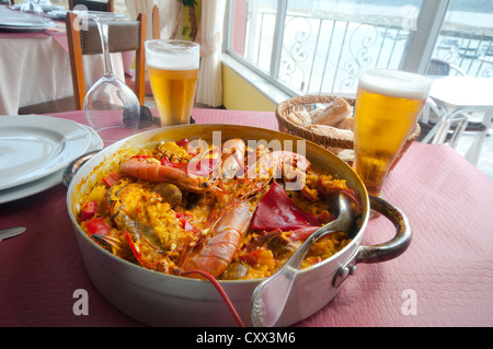 Spanische Paella für zwei Personen mit frisch gefangenen Garnelen, Krabben und Krebse.  In einem Restaurant am Meer mit Bier und Brot. Stockfoto