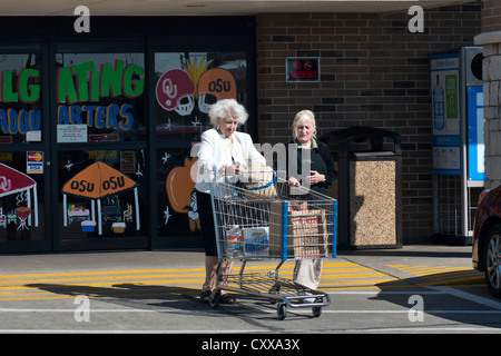 Eine weibliche Store Mitarbeiter hilft, eine alte Frau mit ihrem Warenkorb verlassen ein Supermarkt in Oklahoma City, Oklahoma, USA. Stockfoto