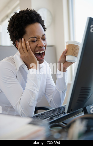 Afroamerikanische Frau Gähnen am Schreibtisch Stockfoto