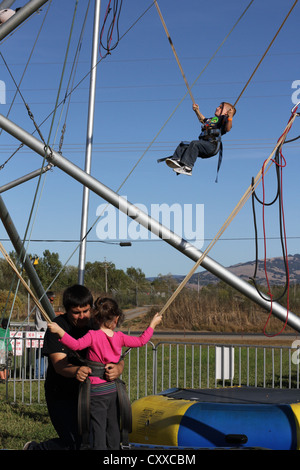 Ein kleines Kind immer angeschnallt in einem Geschirr für ein Bungee-Bounce Spiel. Stockfoto
