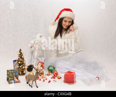 Junge Frau mit Weihnachtsmütze und einem weißen Webpelzjacke von Weihnachtsschmuck umgeben Stockfoto