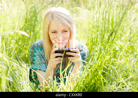 Junge Frau sitzt in hohe Gräser auf einer Wiese, die Kommunikation per Handy, smartphone Stockfoto