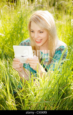 Junge Frau sitzt in hohe Gräser auf einer Wiese spielen eines Computerspiels Stockfoto